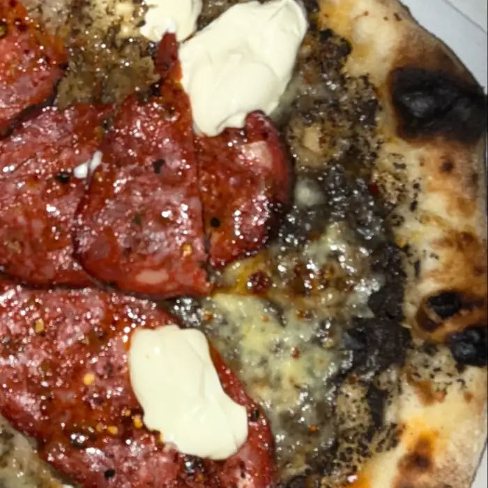 Kawałek pizzy z salami, zielonym pesto i białym serem